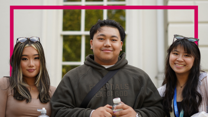 Three students - two female, one male - smiling warmly to camera outside a university building