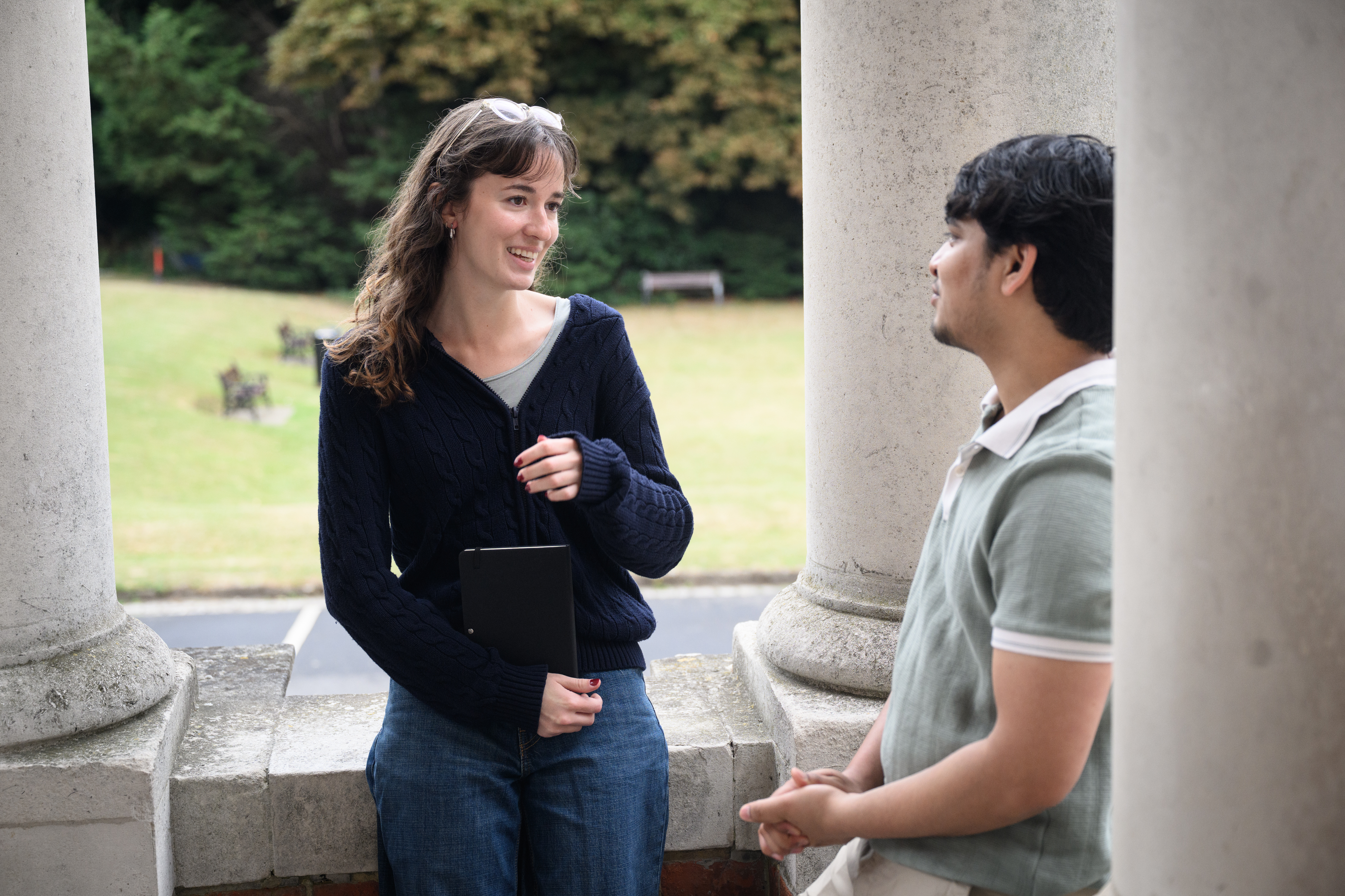 two students in conversation smiling outside of university building