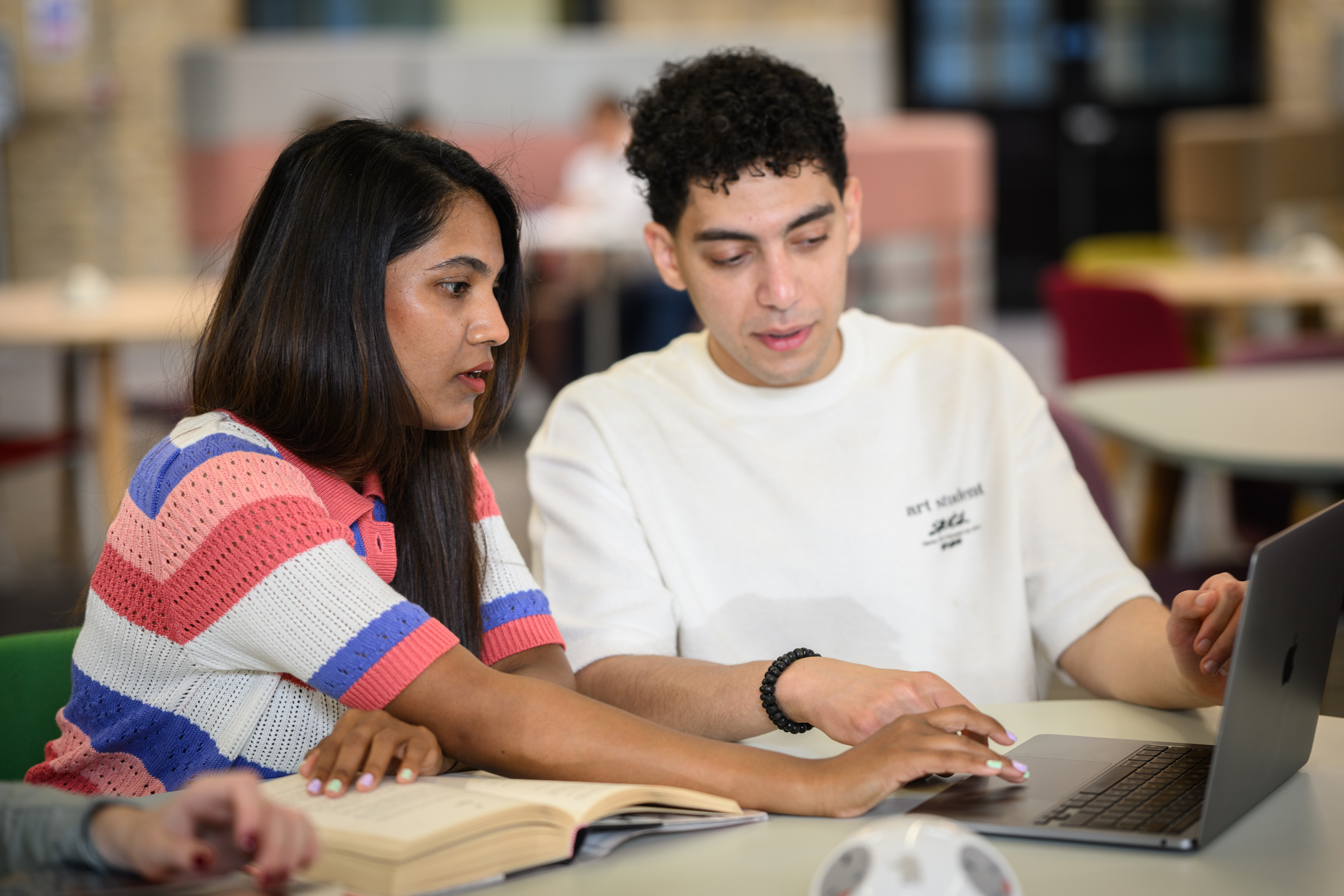 two students sharing a laptop and reading a book