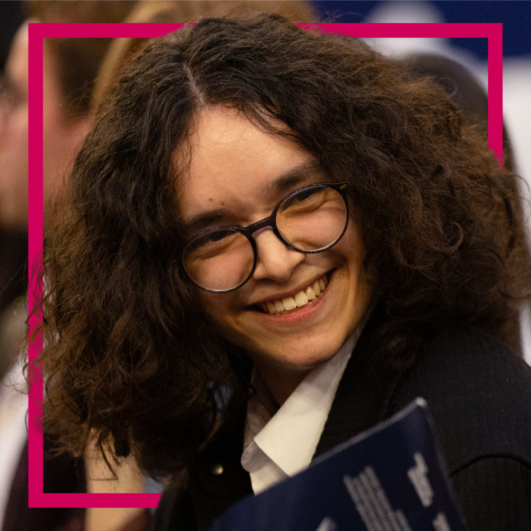 student wearing glasses, in a crowd smiling