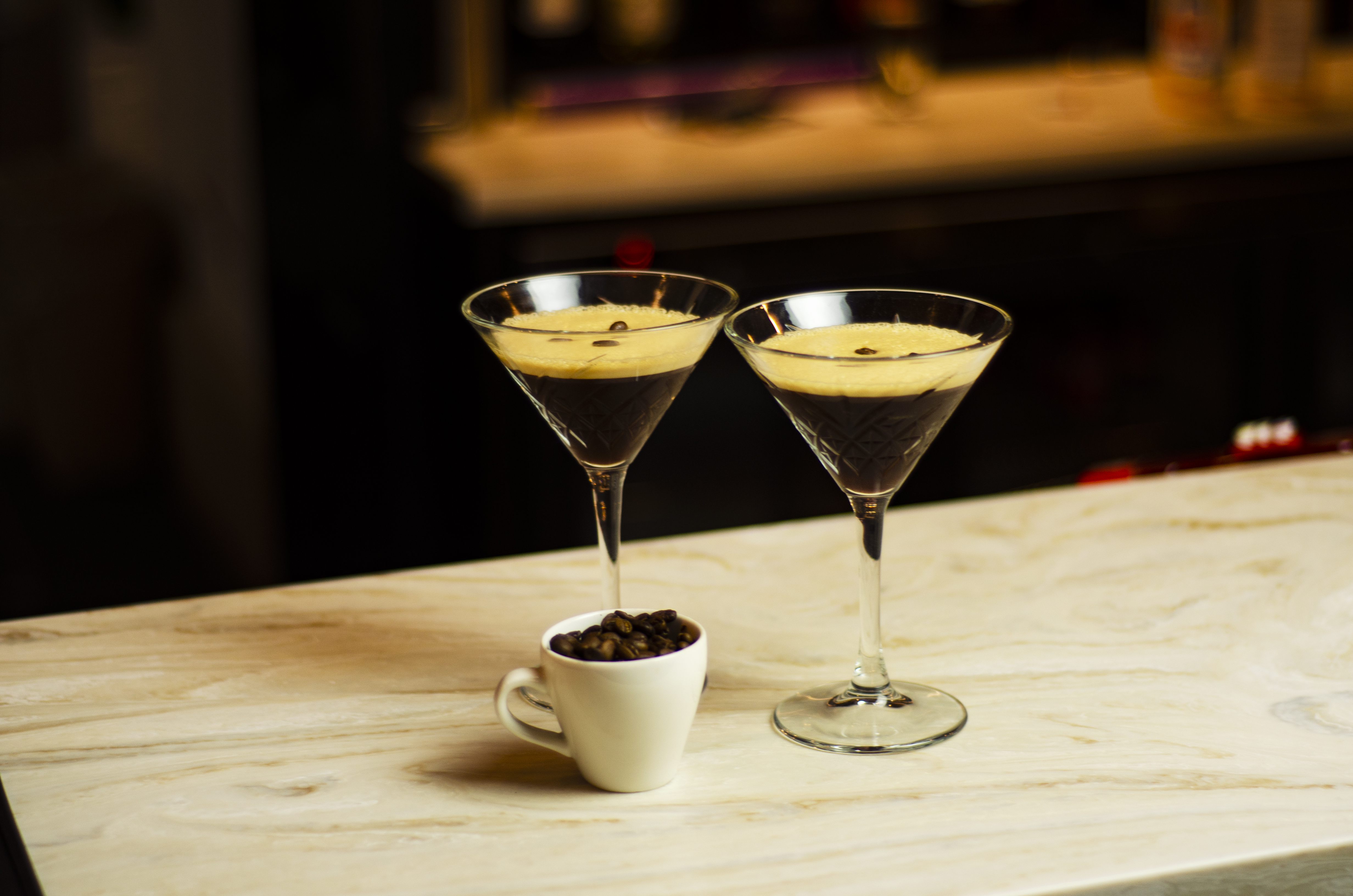 two espresso martinis photographed on the bar in low lighting