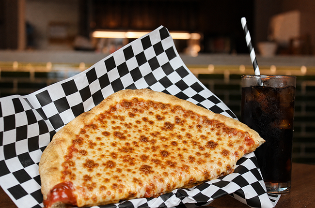 Half circle shaped pizza topped with cheese, beside a glass of coca cola