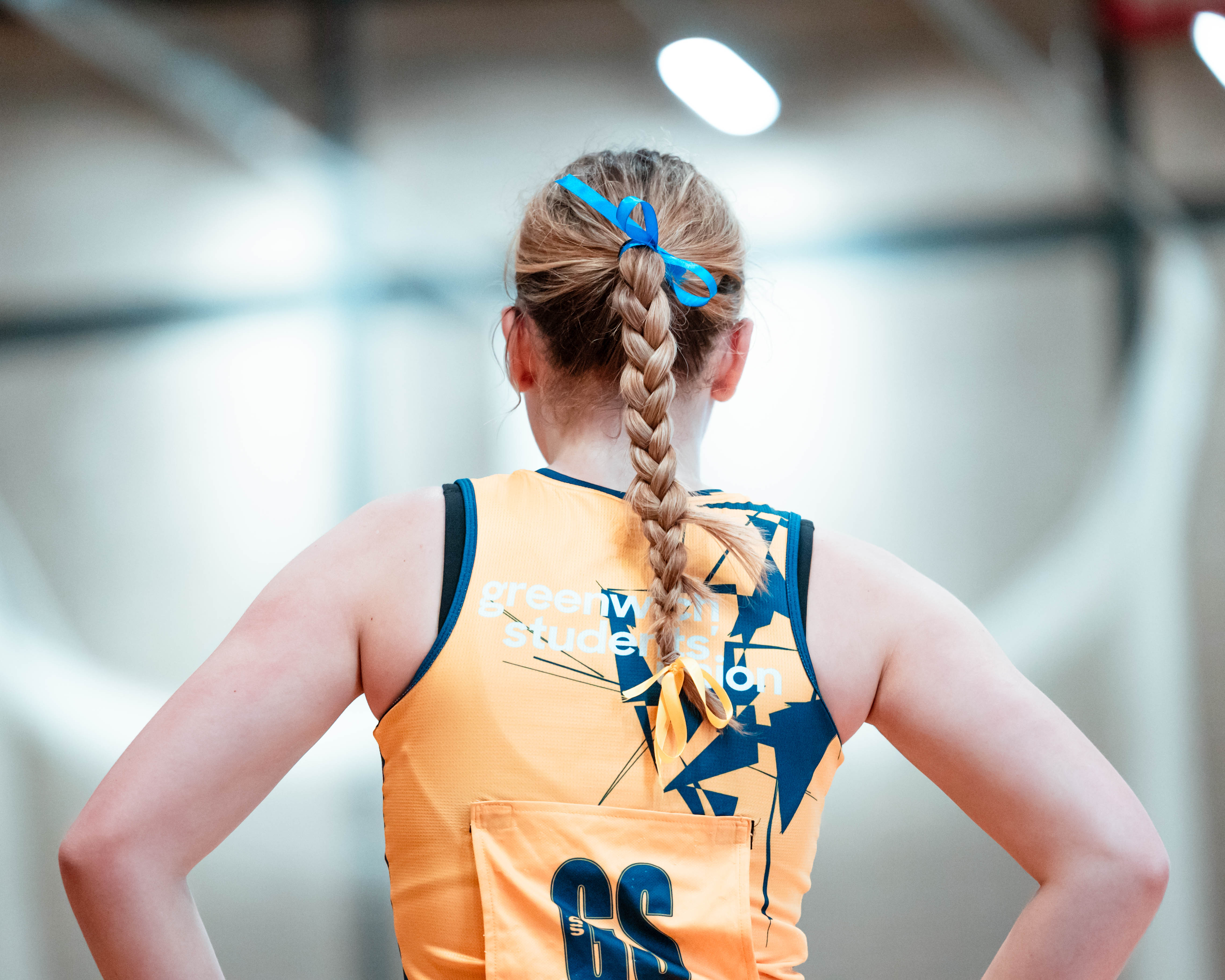 photo of netball player from behind, she is standing in power pose with her hands on her hips. You can see the back of her kit
