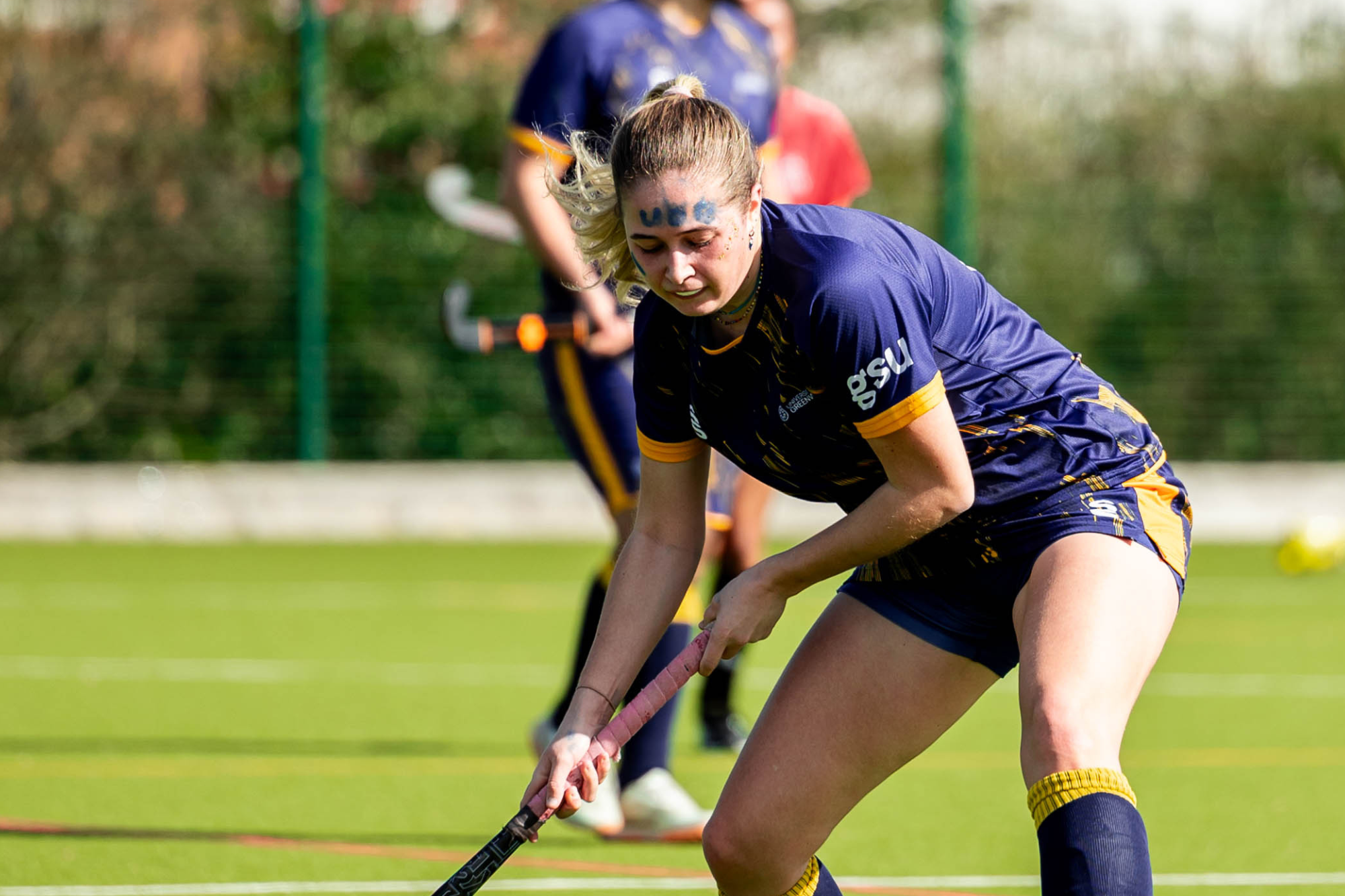 hockey player bent down slightly with her hockey stick guiding the ball mid game