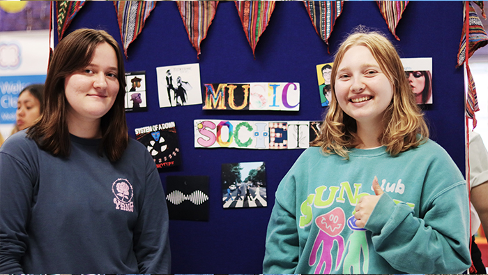 Two young female students smiling to camera, one giving a thumbs up