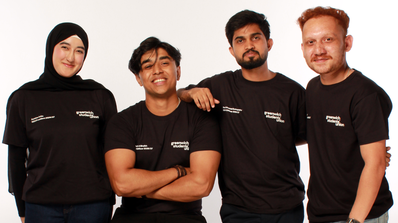 the 4 officers in a studio setting leaning on each other and smiling towards the camera