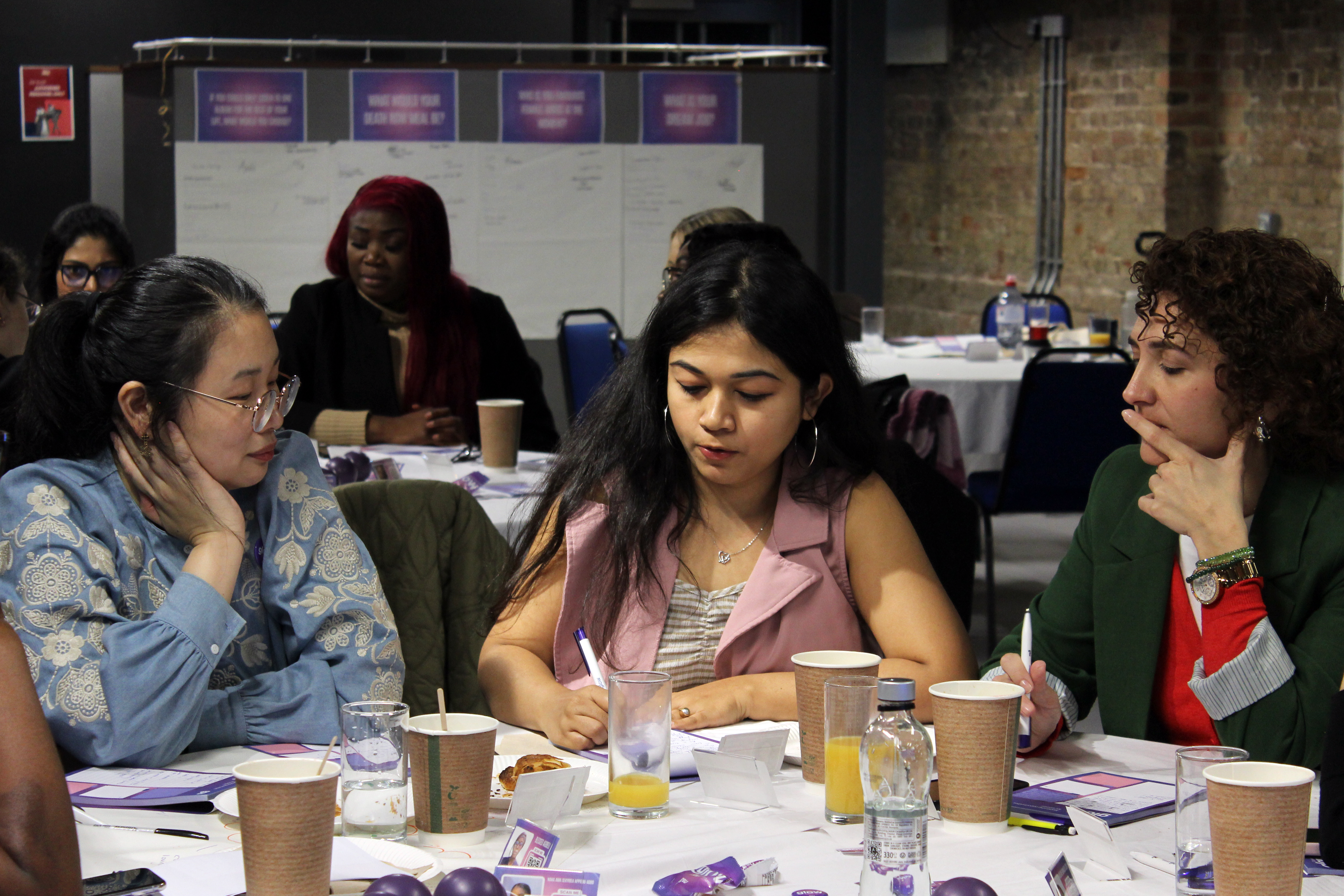 group of three female students around a table writing and discussing